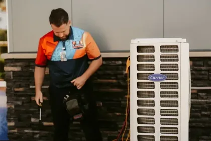 An RJ Kielty HVAC technician in a branded uniform preparing tools to service a Carrier outdoor air conditioning unit