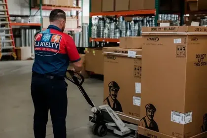 An RJ Kielty technician using a pallet jack to move Lennox HVAC equipment in a well-organized warehouse