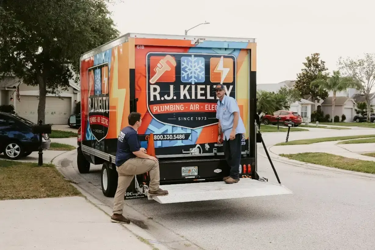 Two RJ Kielty technicians preparing to unload equipment from a large branded service truck parked on a residential street for a home service call