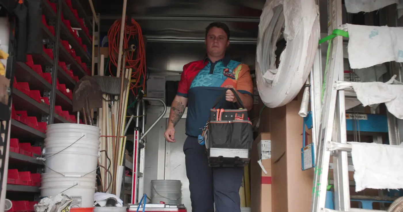 A technician lifting his tool bag from a fully stocked R.J. Kielty service van