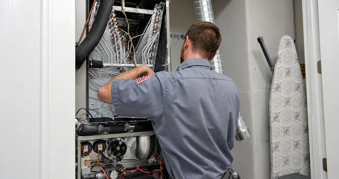 A technician inspecting the wiring and controls inside an opened furnace cabinet