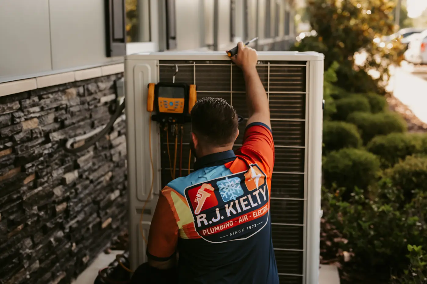 A technician checking system pressures with gauges connected to an outdoor condenser
