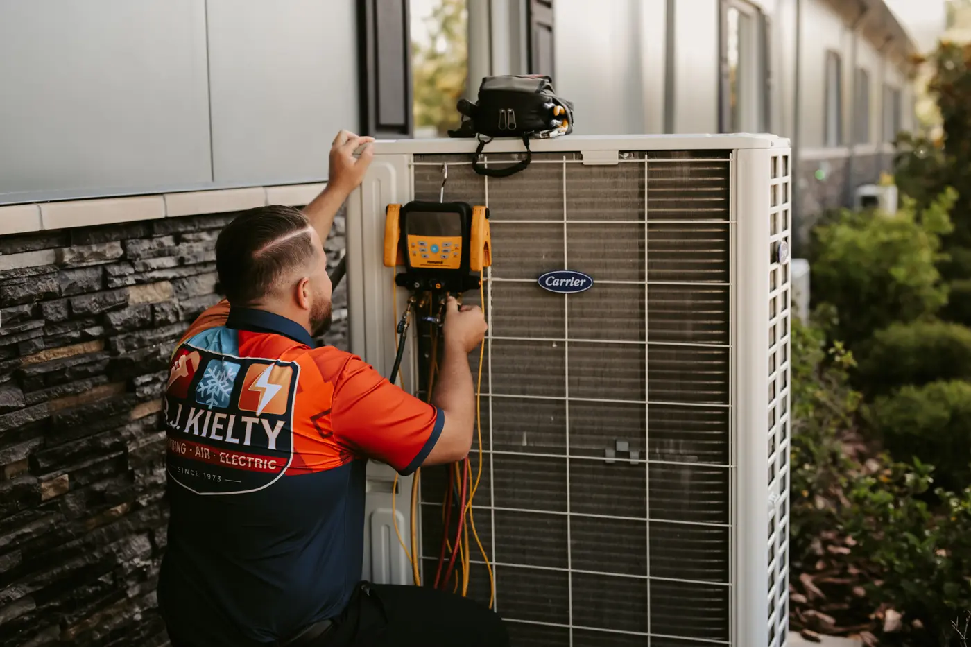 A technician connecting diagnostic gauges to an outdoor Carrier condenser