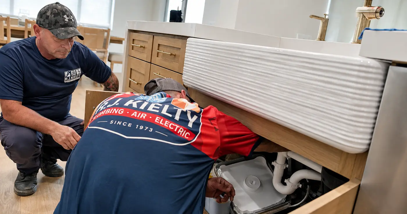 A plumber inspecting and repairing the pipework under a kitchen sink