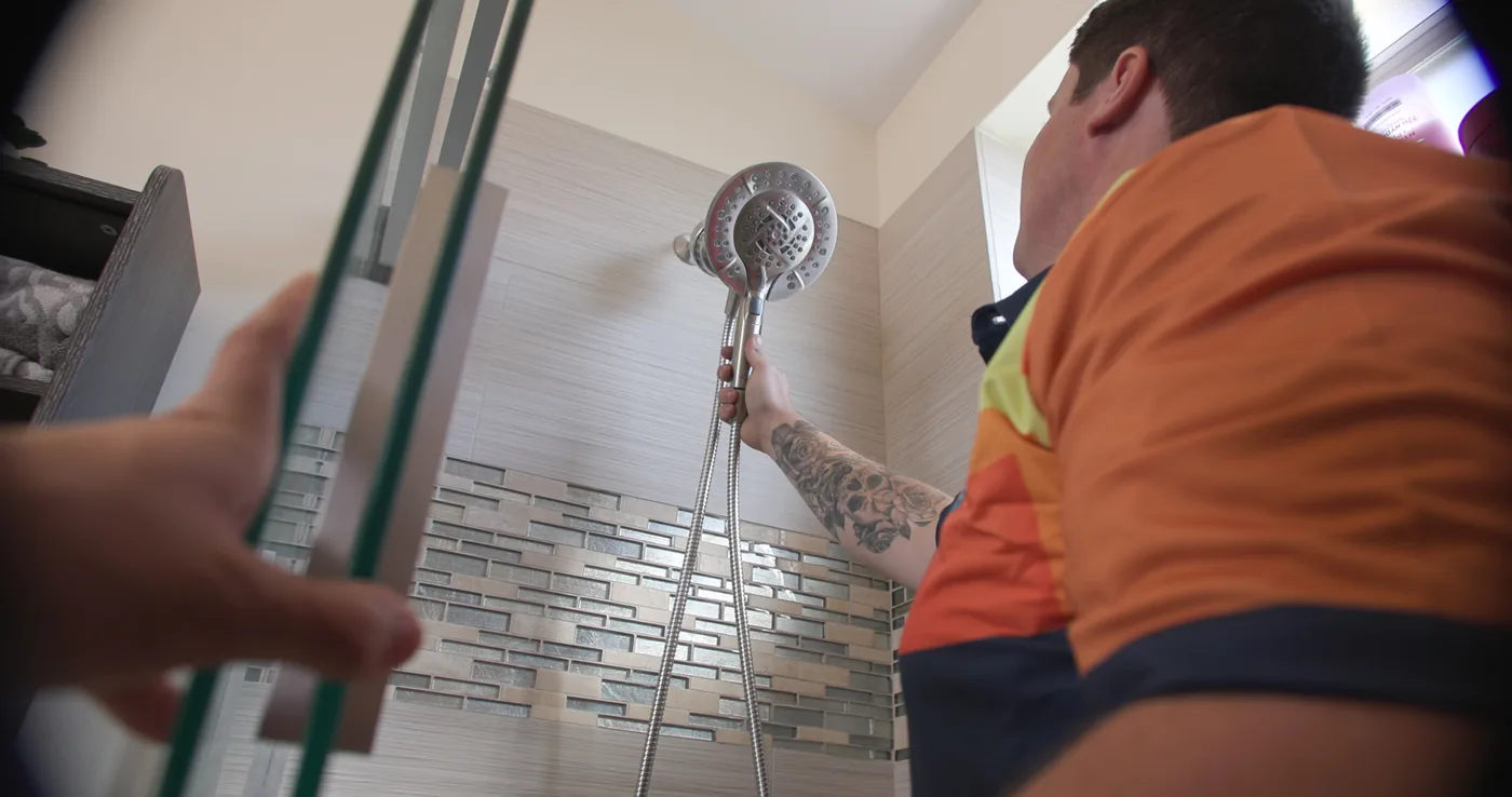 A technician fitting a handheld shower and slide bar in a newly tiled shower