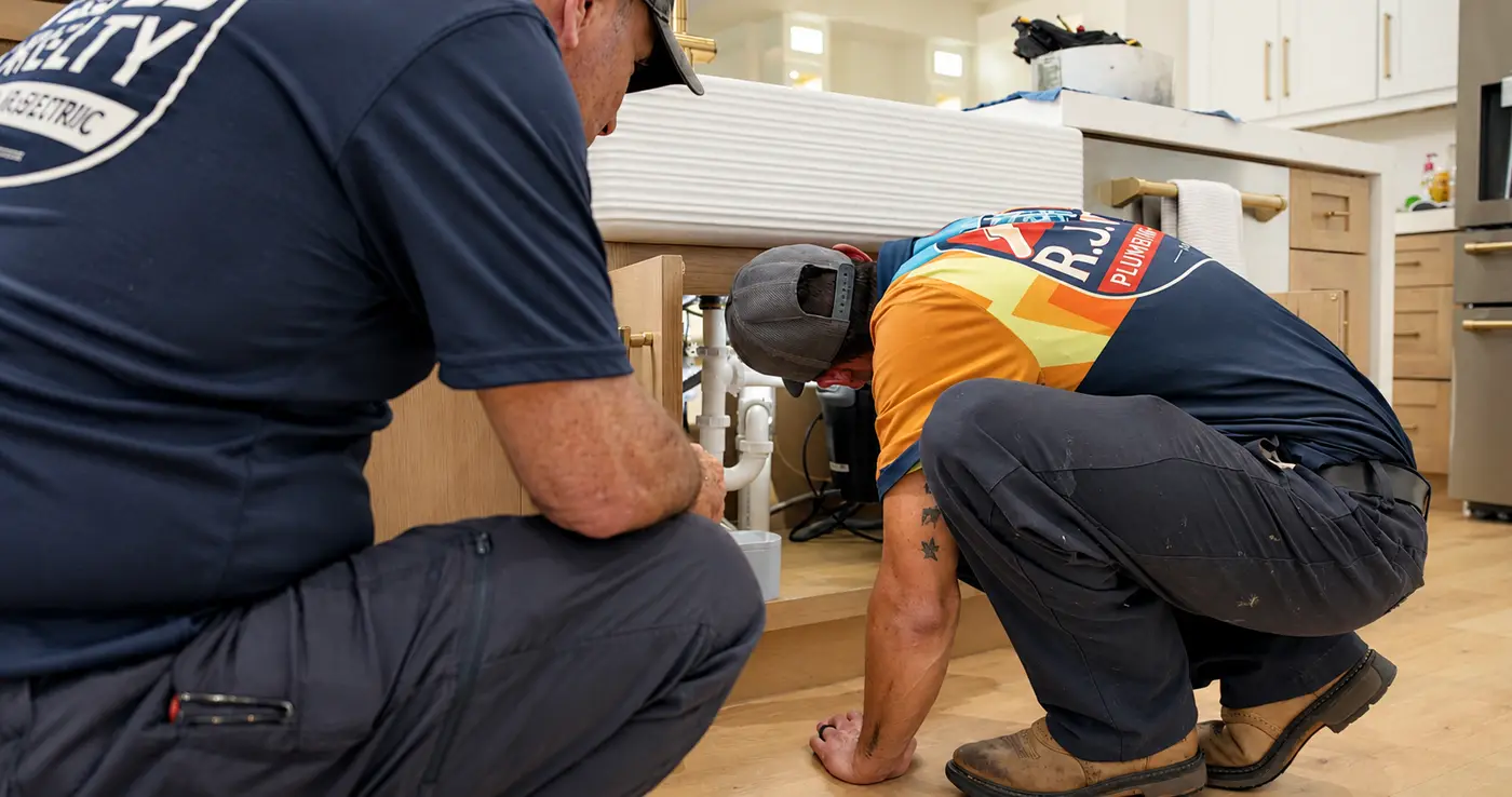 Two R.J. Kielty technicians inspecting the drain lines and connections beneath a kitchen sink
