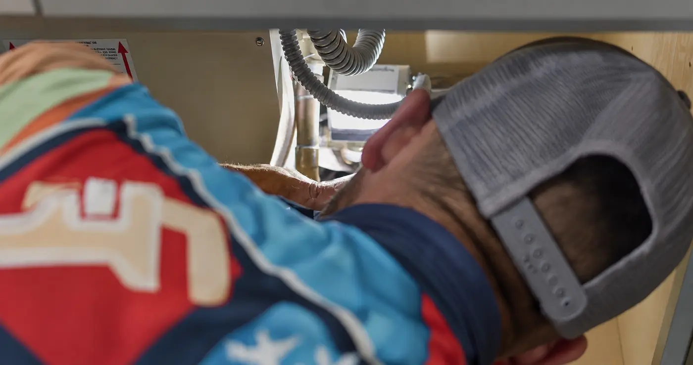 A technician repairing plumbing connections in the cabinet space beneath a sink